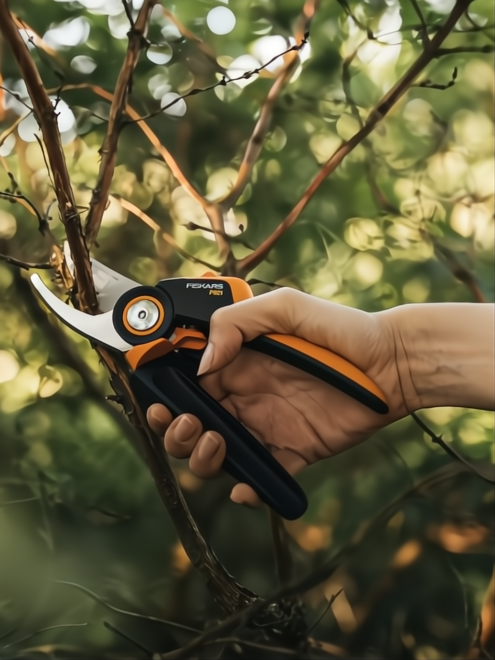 Mano podando ramas con tijera Fiskars X-Series P921 negra y naranja, hoja afilada.