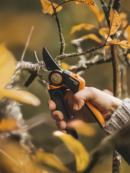 Tijera de podar Fiskars X-Series P961 negra y naranja, con hoja de acero templado, cortando una rama.