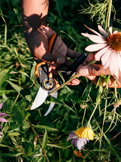 Mano podando una flor con tijera Fiskars X-Series P961 negra y naranja con hoja de acero.