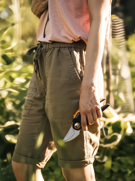 Persona con shorts caqui y camiseta rosa claro sosteniendo una tijera de podar Fiskars X-Series P961.