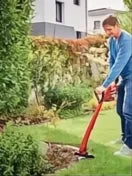 Hombre usando un recortabordes Einhell GC-CT 18/24 Li P-Solo naranja y negro en un jardín.