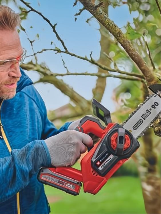 Hombre usando motosierra FORTEXXA roja y negra para podar un árbol.