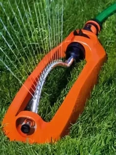 Aspersor oscilante naranja de plástico con barra metálica rociando agua sobre césped verde.