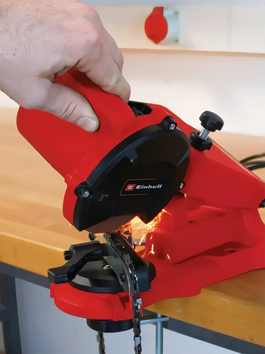 Red Einhell GC-CS 85E chainsaw sharpener in use, sparks flying as it sharpens a metal chain.